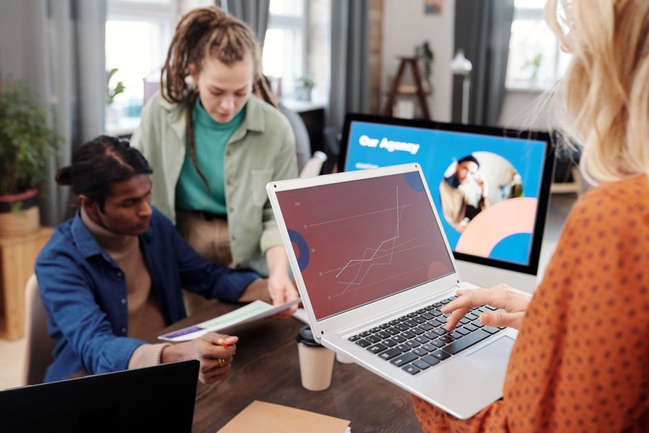 Grupo de profissionais colaborando em um escritório moderno usando laptops e discutindo ideias.